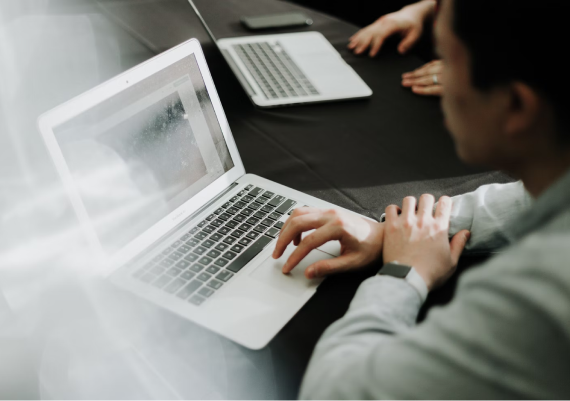A high-angle, slightly blurred shot of a person using a silver laptop on a dark table