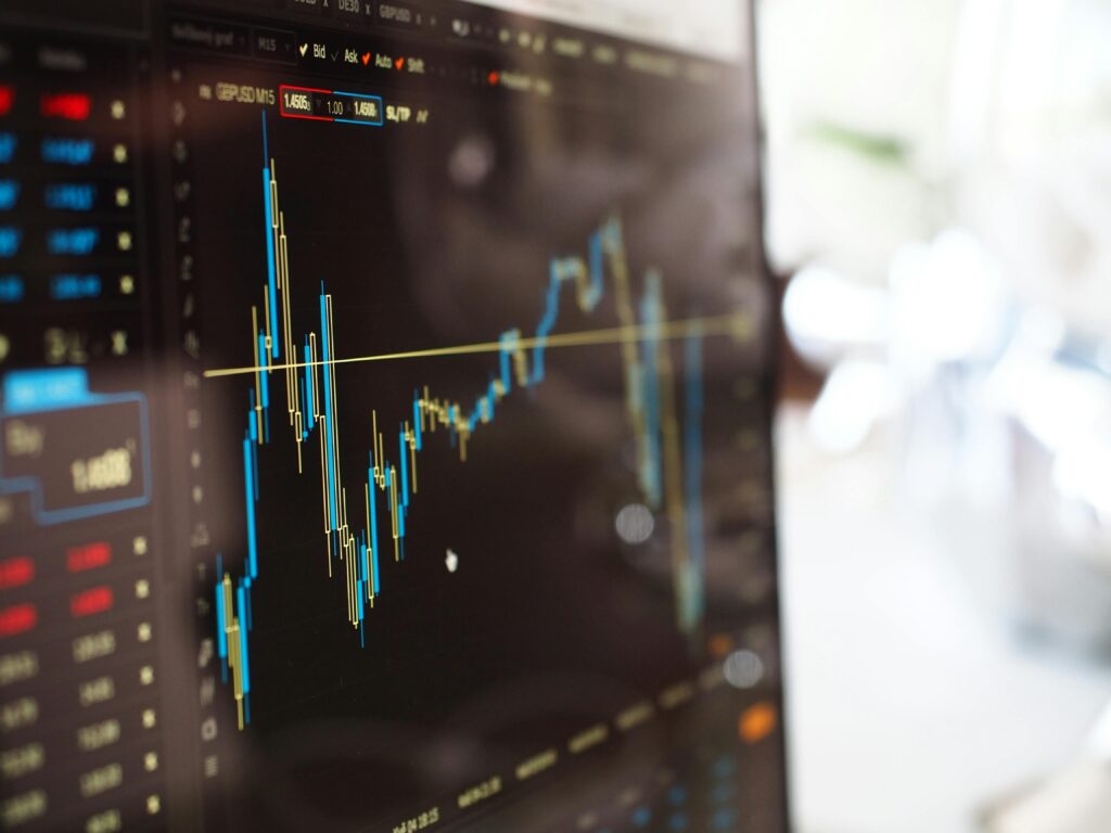 A close-up, angled view of a computer screen displaying a financial candlestick chart with blue and yellow bars representing stock market or currency fluctuations.