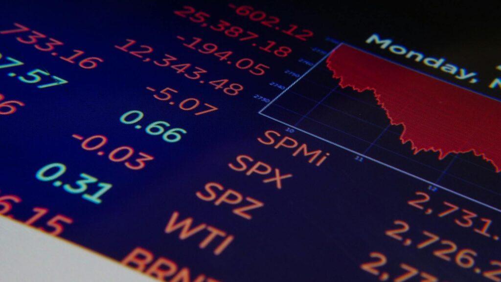 A close-up of a digital screen displaying stock market tickers and a red line graph trending downward, indicating a market decline.