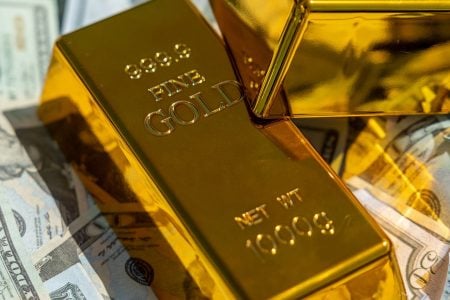 Two gold bars resting on a pile of US dollar bills, representing a portfolio shift towards real assets during a monetary reset.